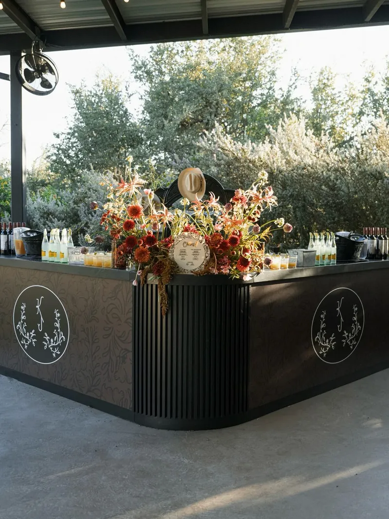 Outdoor ranch bar with custom monogram signage and an autumn floral arrangement