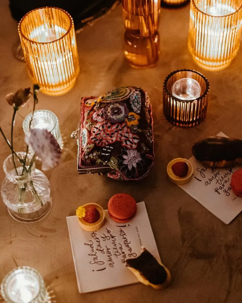 Hand-calligraphed place card by candlelight beside macarons and an embroidered box