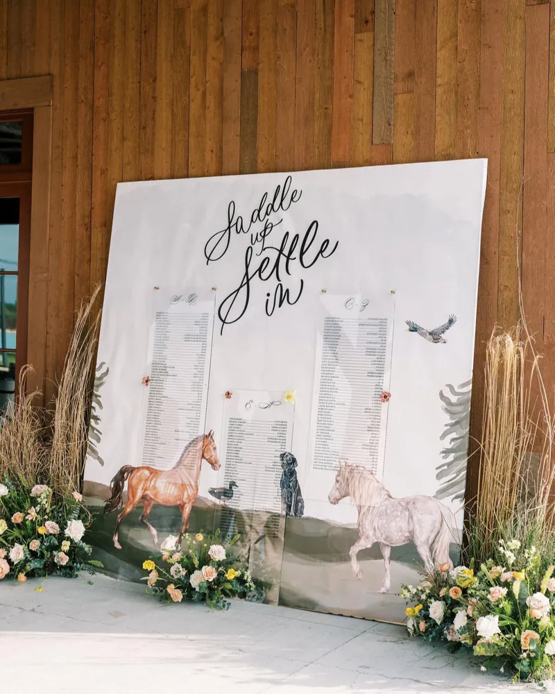 "Saddle up & settle in" seating chart with painted horses and calligraphy, framed by wildflowers